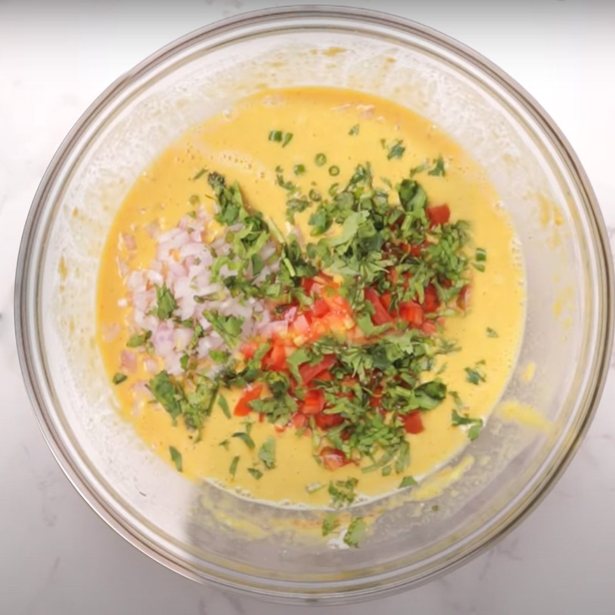 adding vegetables in a glass bowl in a batter